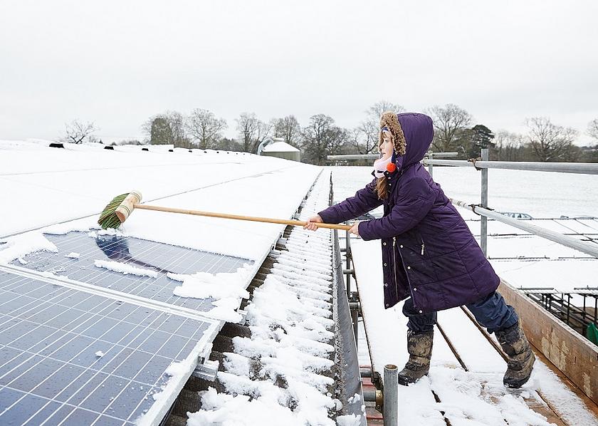 Mädchen fegt mit einem Besen den Schnee von einer Solardachanlage