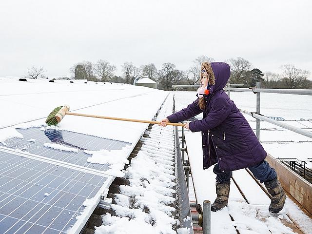 Mädchen fegt mit einem Besen den Schnee von einer Solardachanlage
