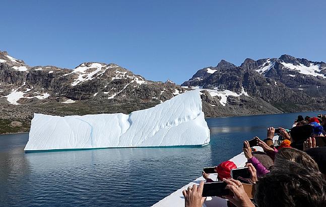 Touristen auf einem Schiff fotografieren mit ihren Smartphones einen kleinen treibenden Eisberg