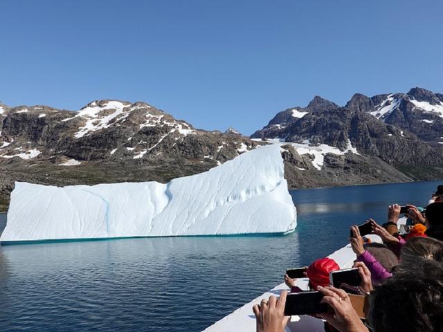 Menschen auf Boot fotografieren einen kleinen schmelzenden Eisberg im Wasser