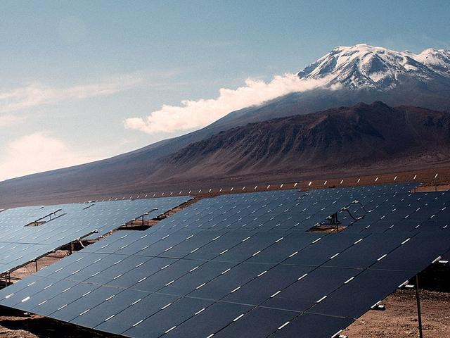 Solaranlage in chilenischer Wüste, im Hintergrund schneebedeckter Vulkankegel