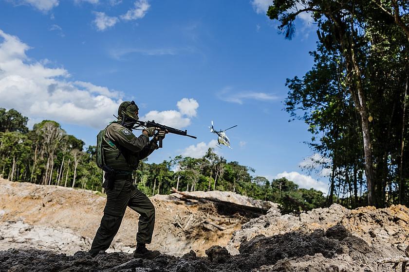 Bewaffneter Mann im gerodeten Regenwald und Hubschrauber in der Luft