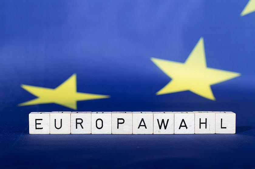 Beschriftete Bausteine mit Buchstaben, die zusammen "Europawahl ergeben. Im Hintergrund Teile der europäischen Flagge.