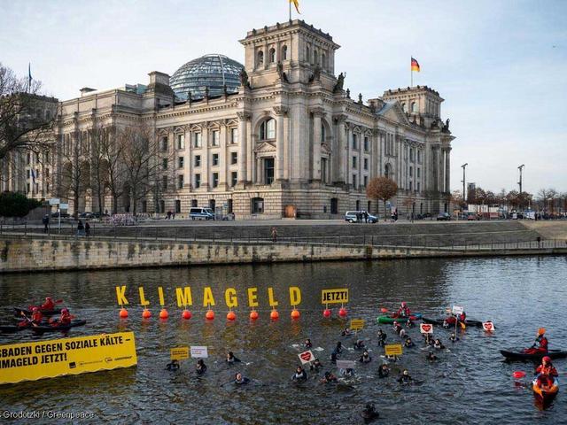 Menschen in Neopren vor Reichstag in der Spree mit Transparenten zum Klimageld