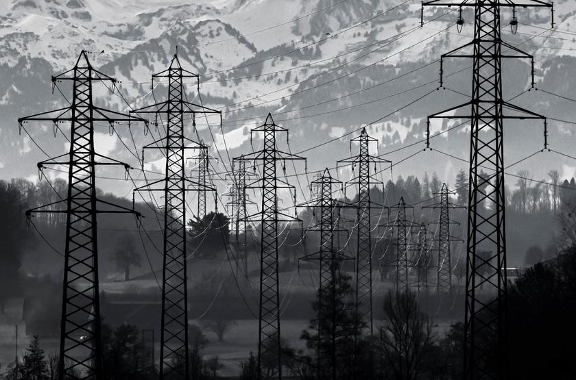 Schwarz-weiß Bild mehrerer Stromleitungen und Masten, mit schneebedeckten Bergen im Hintergrund