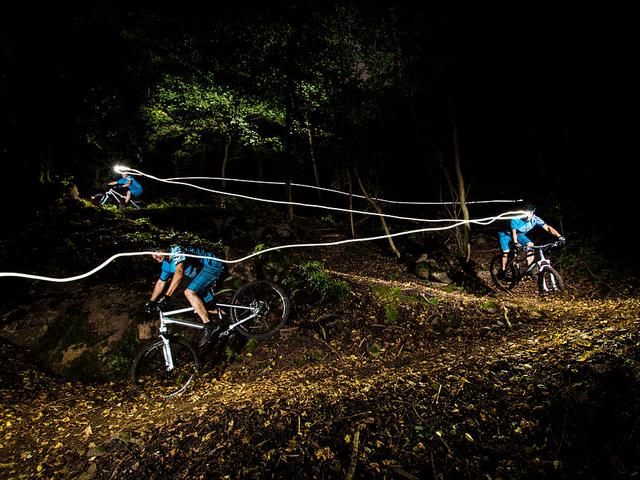 drei Fahrradfahrer bei Nacht auf einem Waldweg, Kopflampen hinterlassen Lichtspur