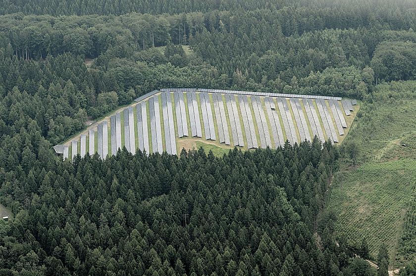 Luftaufnahme einer großflächigen Solaranlage umgeben von Wald.