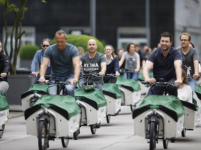 Frauen und Männer fahren auf E-Lastenrädern durch die StadtFrauen und Männer fahren auf E-Lastenrädern durch die Stadt