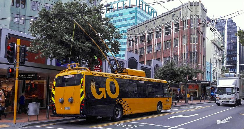 Ein gelber Bus in einer Straße einer Stadt an einer Oberleitung.