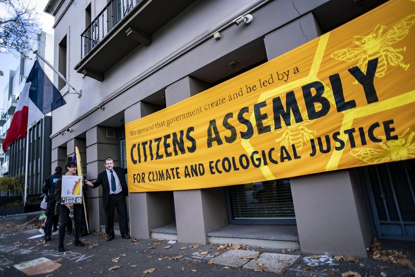Ein Banner vor einem Gebäude mit französischer Flagge. Auf dem Banner steht: "Citizens Assembly - for Climate and Ecological Justice"