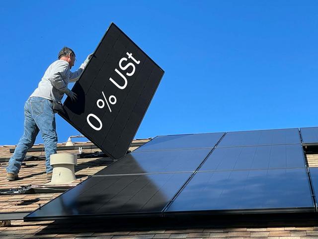 Solarteur balanciert Solarmodul auf einem Dach mit Schriftzug 0 % USt
