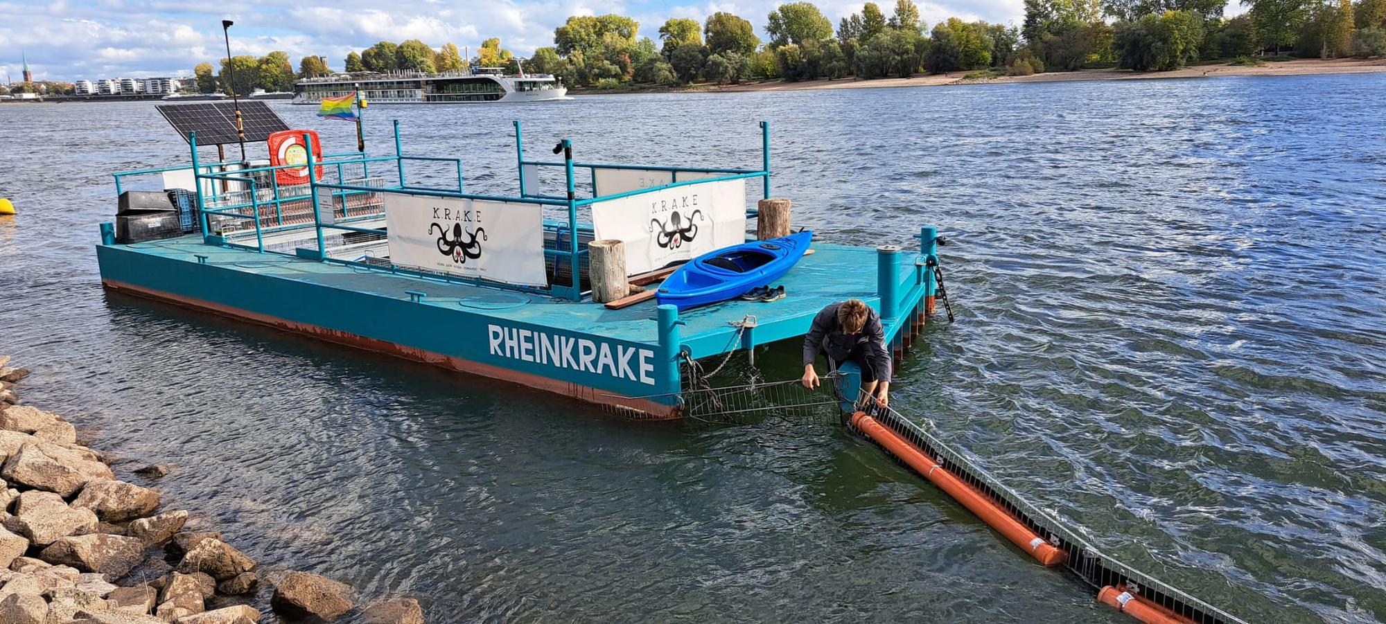 Ein blaues, schwimmendes Konstrukt im Rhein, auf dem "Rheinkrake" steht