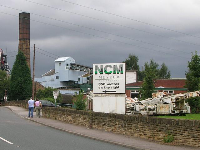 Im Hintergrund ist ein altes Kohlekraftwerk zu sehen. Im Vordergrund ein Hinweisschild auf das naheliegende Museum.
