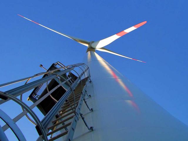 Windkraftanlage von unten mit Leiter und blauem Himmel
