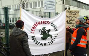 Menschen mit Banner Bürgerinitiative Lebenswertes Rügen vor einem Industriegebäude