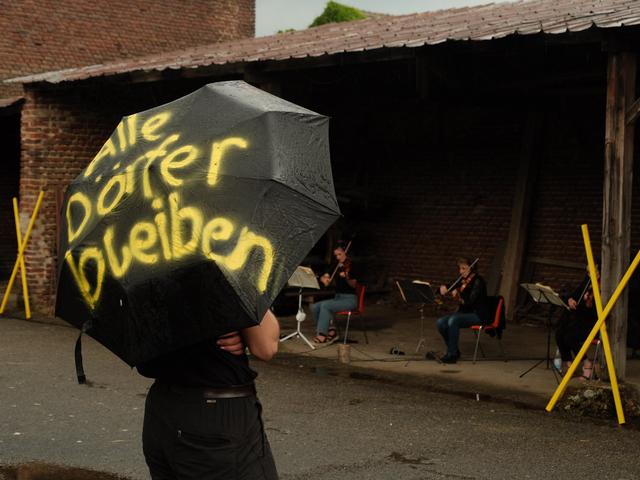 Ein Mensch hält einen Regenschirm, auf dem steht: "Alle Dörfer Bleiben"