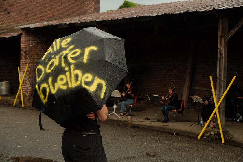 Ein Mensch hält einen Regenschirm, auf dem steht: "Alle Dörfer Bleiben"