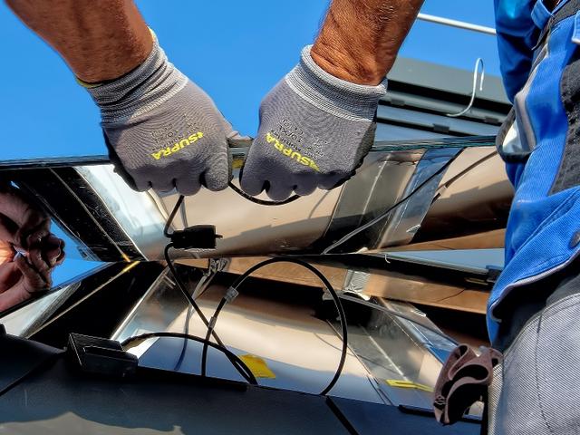Hände von Installateuren beim Bau einer PV-Anlage auf einem Dach