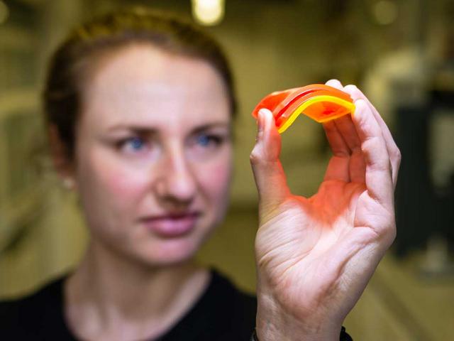Forscherin hält ein Stück leuchtendes gebogenes Kunstoff in der Hand