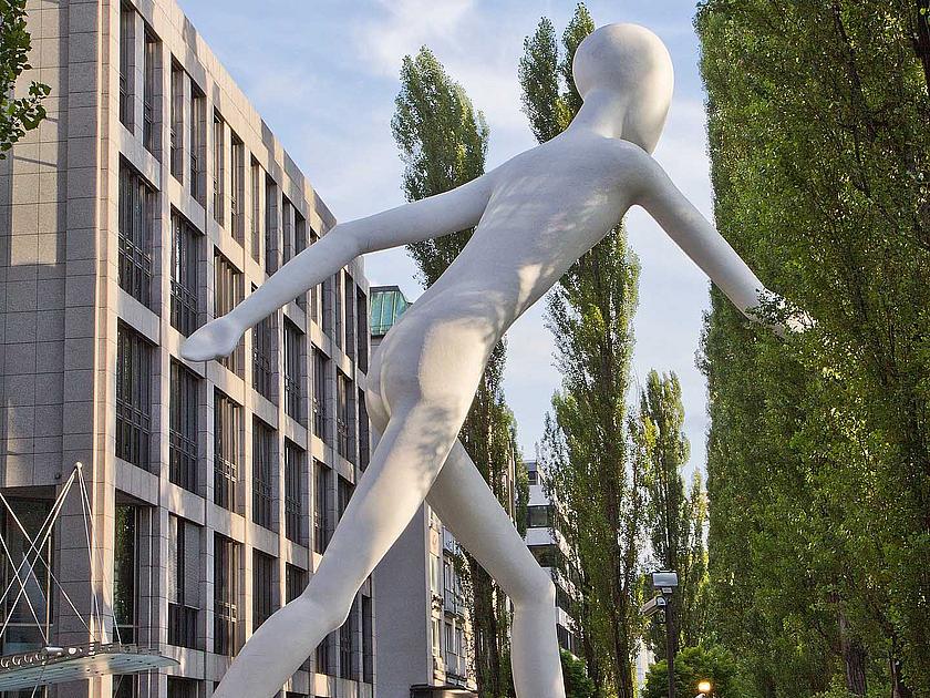 Eine Skulptur einer laufenden weißen Person vor einem verglasten Gebäude.