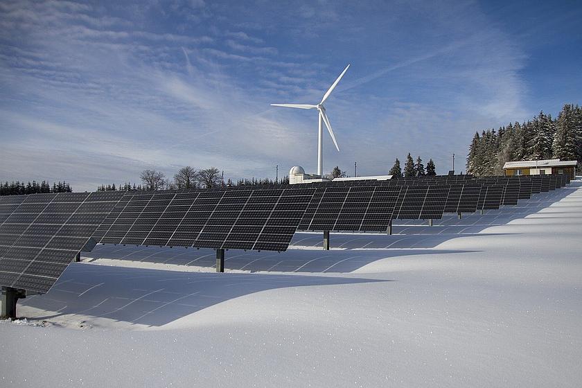 Solarpark im Schnee, im Hintergrund ein Windrad