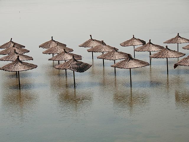 Foto: reedbedeckte Sonnenschirm am Strand, vom Meer überflutet.