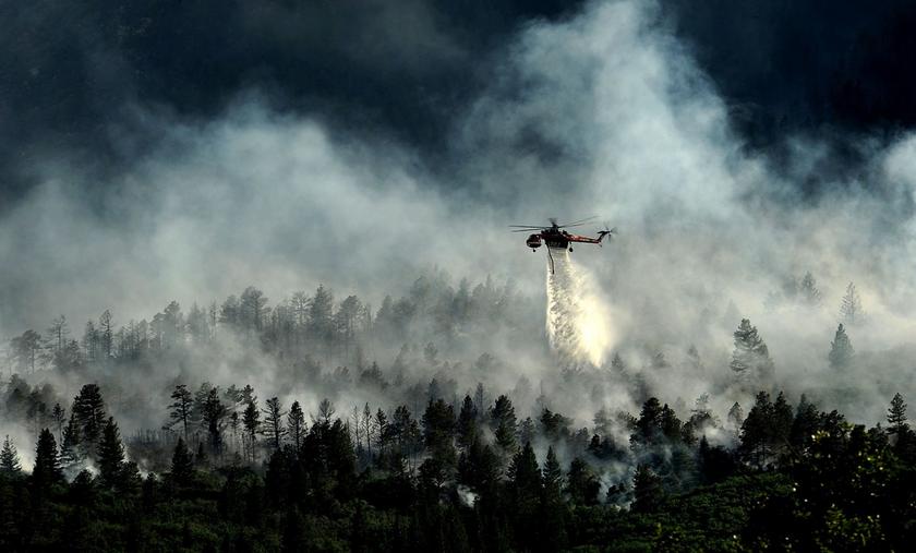 Helikopter fliegt über rauchenden Wald und lässt Wasser ab.