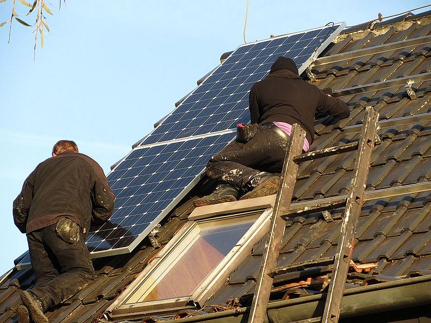 Zwei Arbeiter installieren Photovoltaikmodule auf einem Hausdach