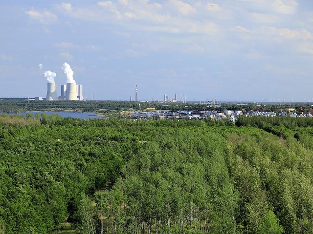 Kraftwerk mit Schornsteinen, daneben Windpark