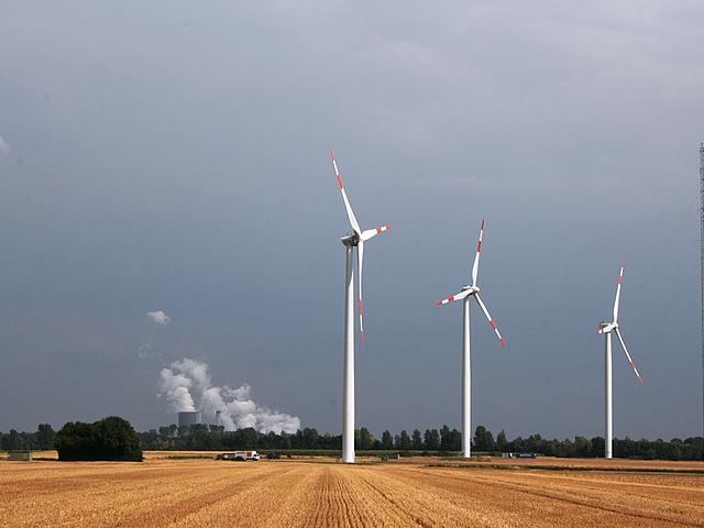 Drei Windkraftanlagen auf freiem Feld und im Hintergrund ein altes Kohlekraftwerk