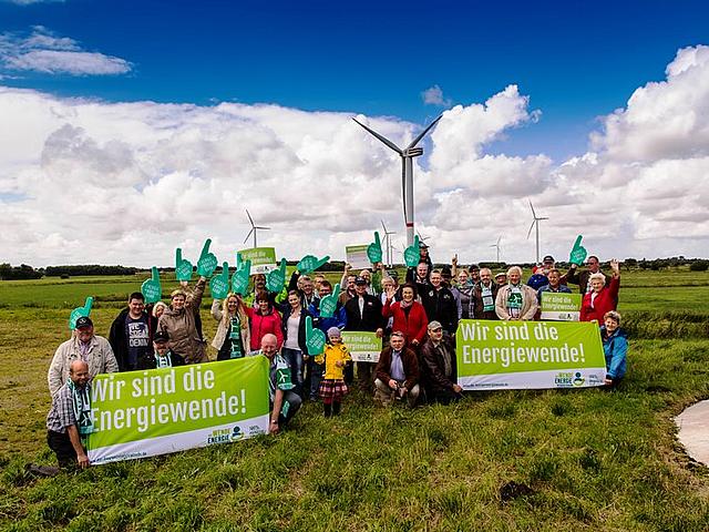 Menschen einer Energiegenossenschaft vor Windrädern