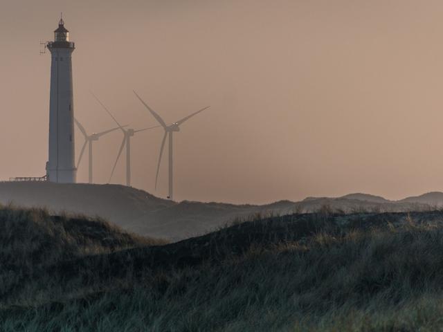 Windenergieanlagen hinter einer Düne und einem Leuchtturm