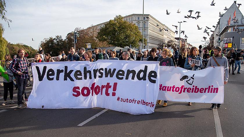Bild einer Demo gegen Autos in der Stadt. Auf einem Banner steht "Verkehrswende sofort" und "#autofreiberlin"