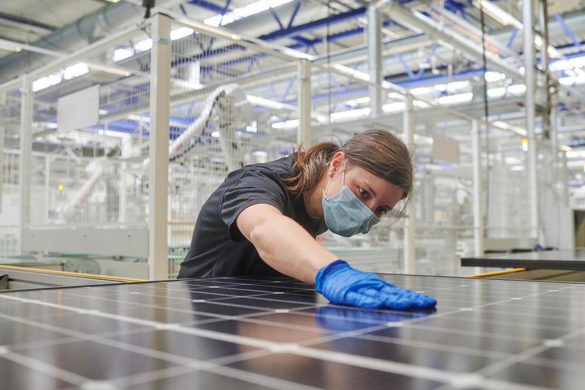 Fabrikarbeiter mit Maske streicht mit der Hand über ein Solarmodul.