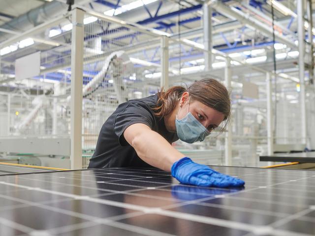 Fabrikarbeiter mit Maske streicht mit der Hand über ein Solarmodul.