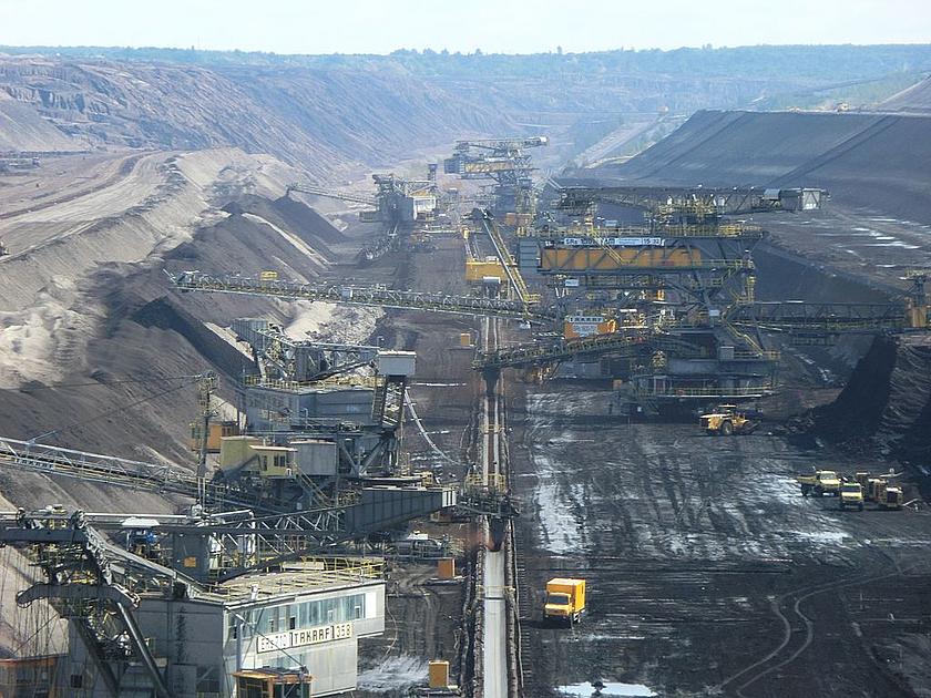 Blick auf den Tagebau mit vielen Kohlebaggern, die riesige Mengen an Braunkohle fördern, welches auf einem Band in der Mitte des Tagebaus abtransportiert wird.