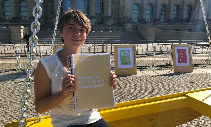 Lea Nesselhauf mit Gesetzpaket in einer symbolischen Waagschale vor dem Berliner Reichstag
