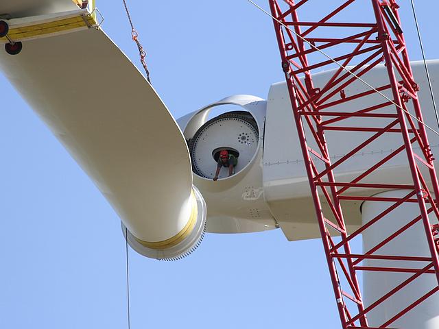 Arbeiter in luftiger Höhe bei Montage eines Windradflügels