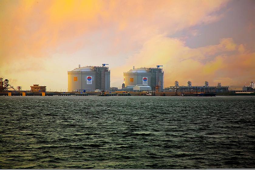 Bild zweier LNG-Terminals (runder Bauten) am Wasser im Sonnenuntergang.