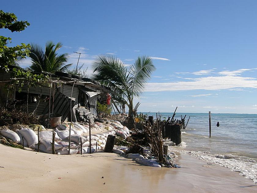 Foto: kleines Haus am Meer, notdürftig mit Sandsäcken vor der herannahenden Flut geschützt
