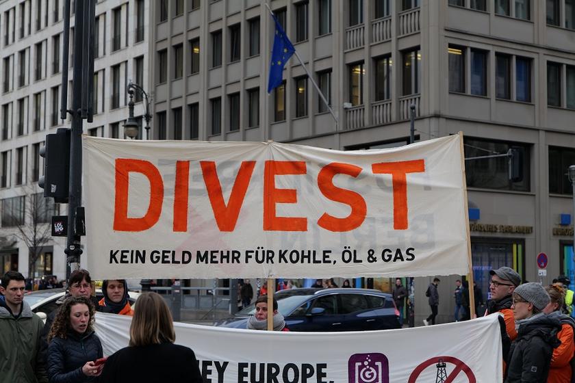 Protest gegen die Förderung fossiler Energien mit Plakat: Divest – kein Geld mehr für Kohle, Öl und Gas