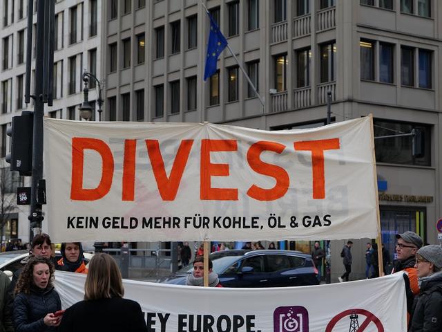 Protest gegen die Förderung fossiler Energien mit Plakat: Divest – kein Geld mehr für Kohle, Öl und Gas
