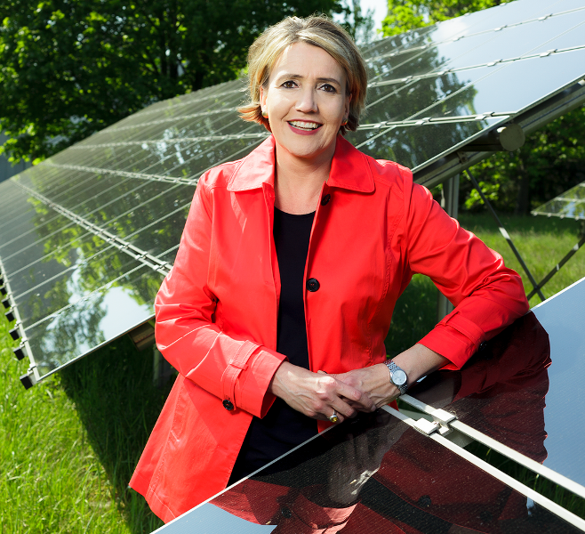Eine Frau mit blonden Haaren und rotem Balzer lehnt an einem Solarmodul