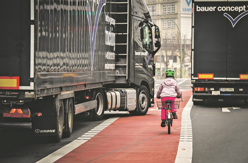 Kind fährt auf einem Fahrradweg entlang und wird von einem großen Lastwagen abgedrängt
