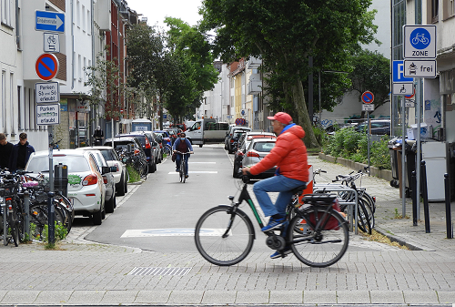 Ein Mann fährt auf einem Fahrrad an einer Straße vorbei, die per Schild als Fahrradzone ausgewiesen ist.
