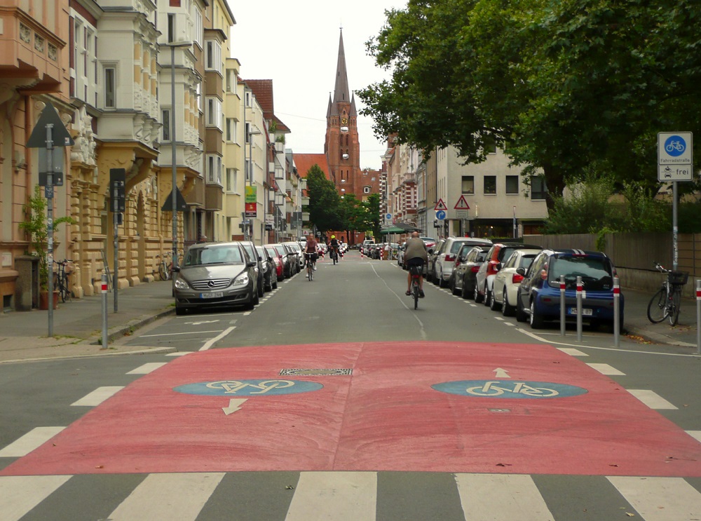 Teils Orange markierte Fahrbahn einer Straße mit Fahrradfahrer:innen