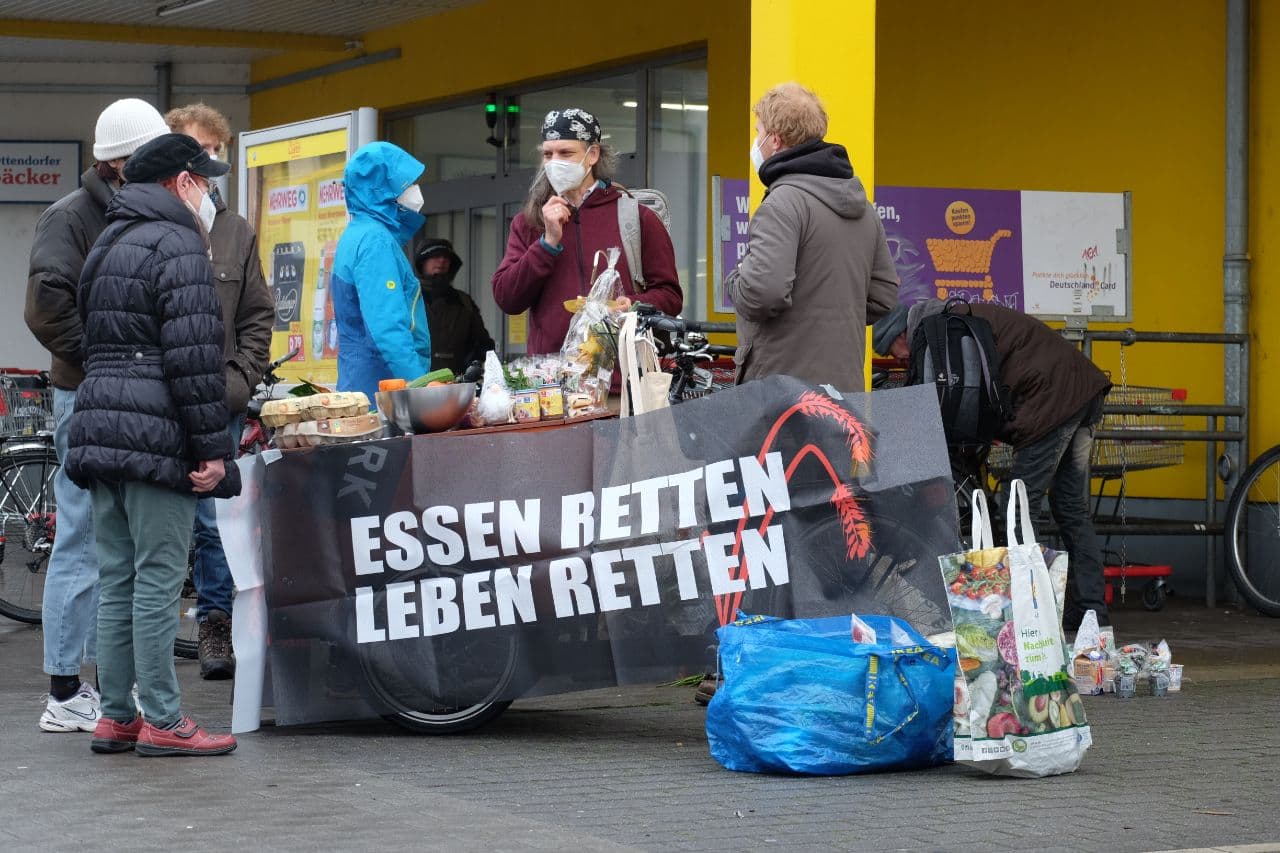 Mann einem Stand mit containierten Lebensmitteln. Auf einem Banner steht "Essen retten - Leben retten"