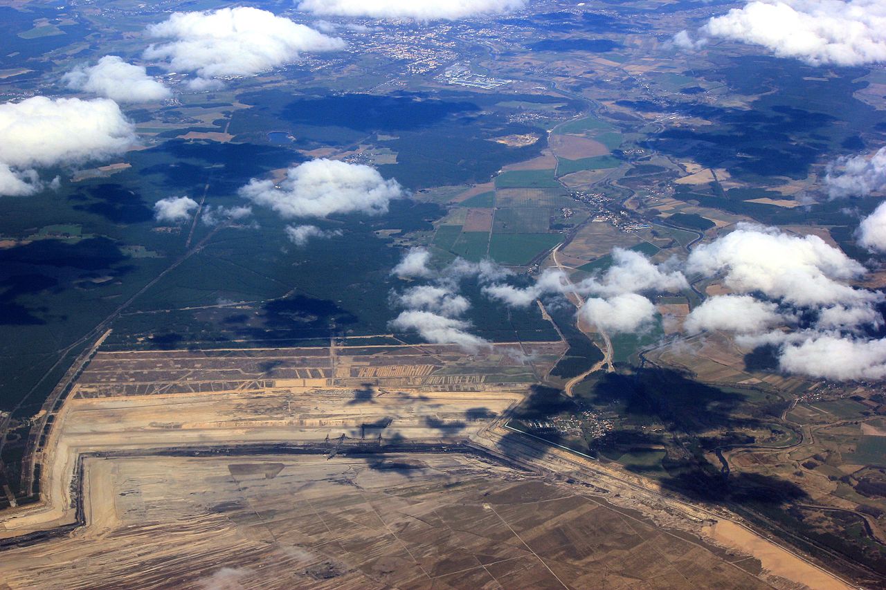 Luftbild eines Tagebaus mit grünen Landschaften nördlich davon.